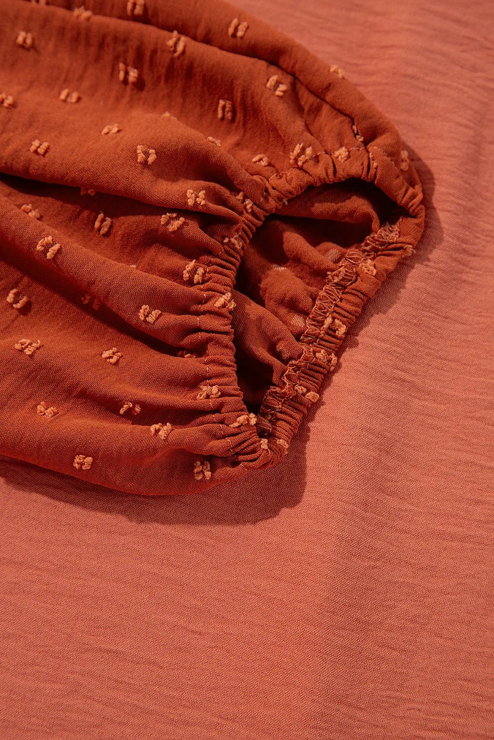 Close-up of the rust Swiss dot blouse fabric showing textured dot details and gathered, elasticized construction along the garment edge.