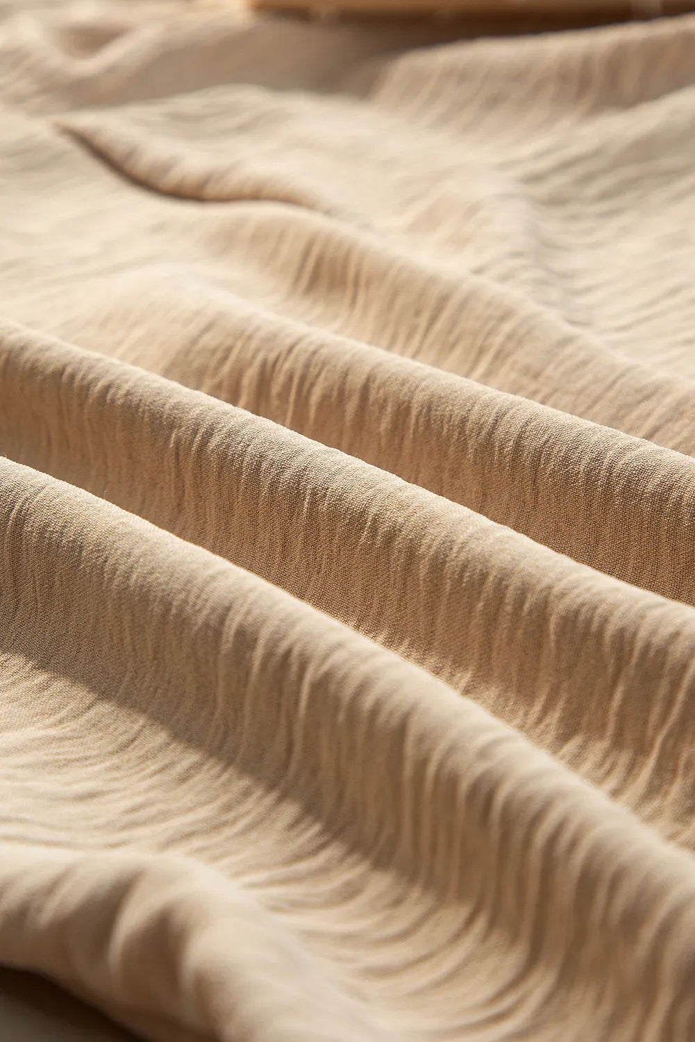 Close-up of beige blouse fabric draped in soft folds, showing its woven texture while the mock neck, balloon sleeves, and silhouette remain out of view.