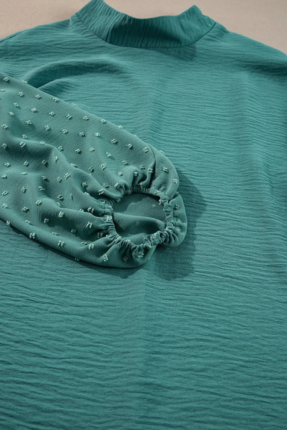 Teal Swiss dot blouse detail showing its gathered mock neck, textured fabric, voluminous balloon sleeve, and elasticized cuff.