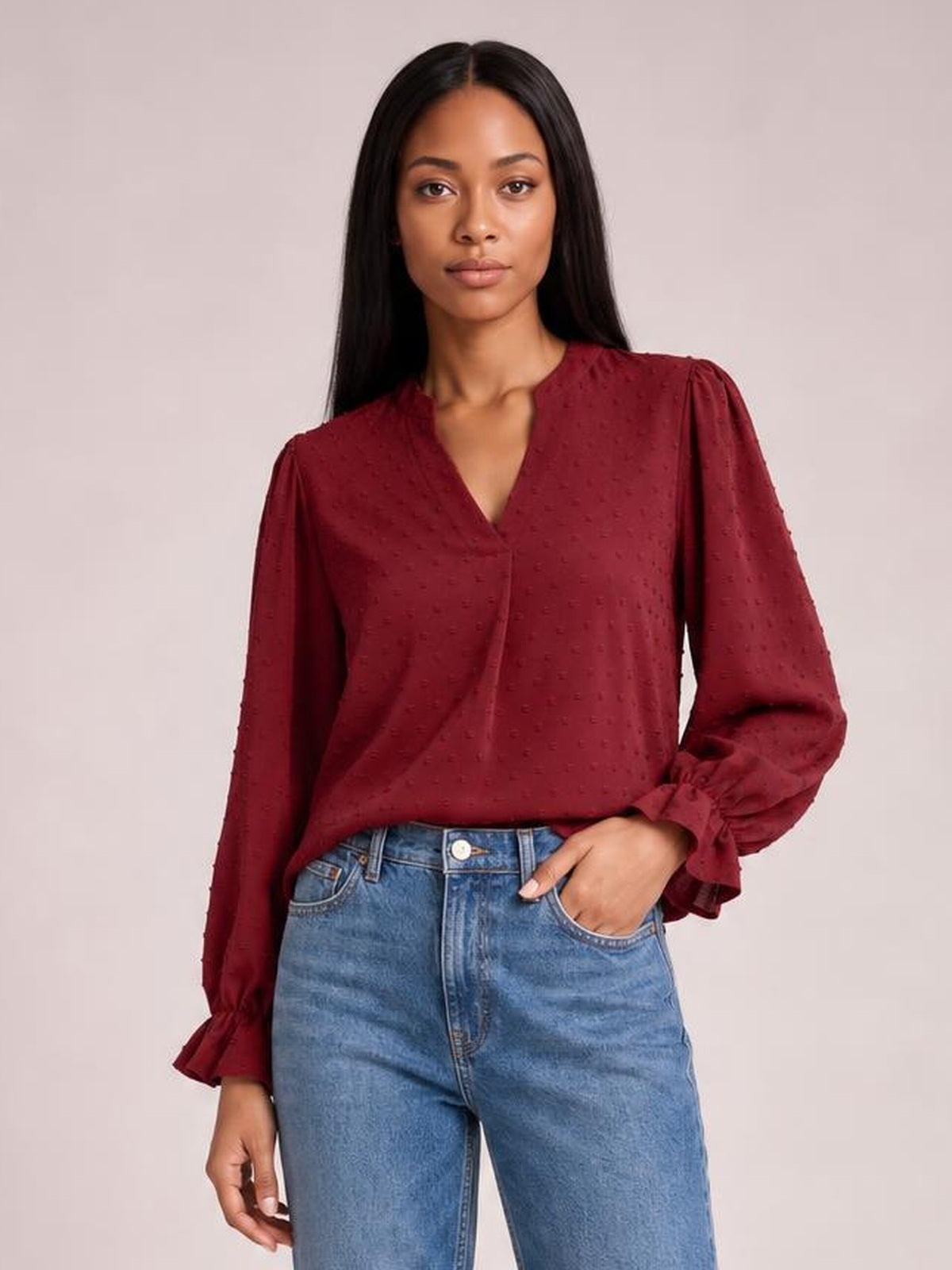 A model poses in a burgundy Swiss dot blouse with a notched V-neck, relaxed long silhouette, and flounce sleeves with gathered cuffs.