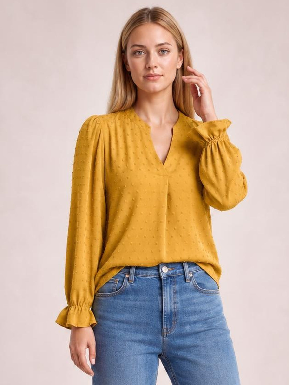 Model wears a mustard Swiss dot blouse with a notched V-neck, relaxed long silhouette, and voluminous long sleeves finished with flounce cuffs.