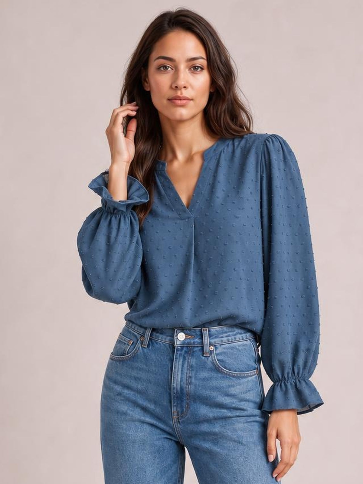 Model wearing a blue Swiss dot blouse with a notched V-neck, relaxed long silhouette, voluminous flounce sleeves, and gathered flared cuffs.