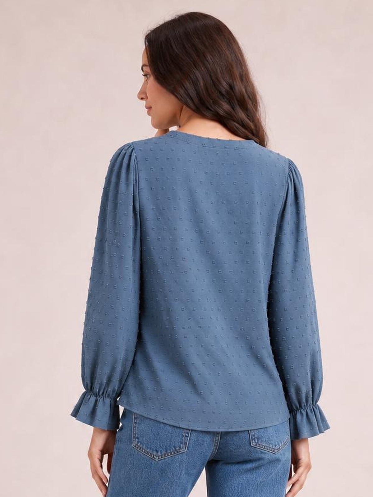 Model shown from the back wears a blue Swiss dot blouse with long sleeves, gathered flounce cuffs, and a relaxed, slightly long silhouette.