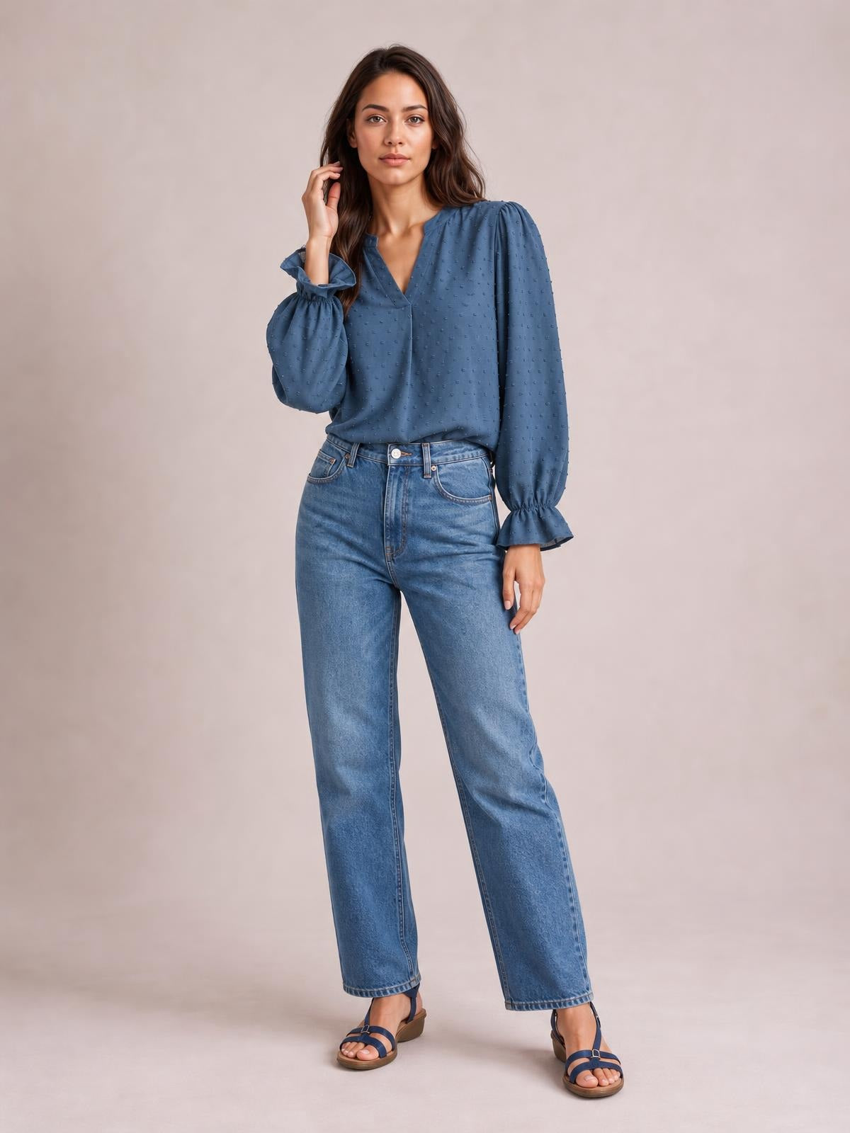 Model poses in a blue Swiss dot blouse with a notched V-neck, long flounce sleeves, gathered cuffs, and a relaxed long silhouette.