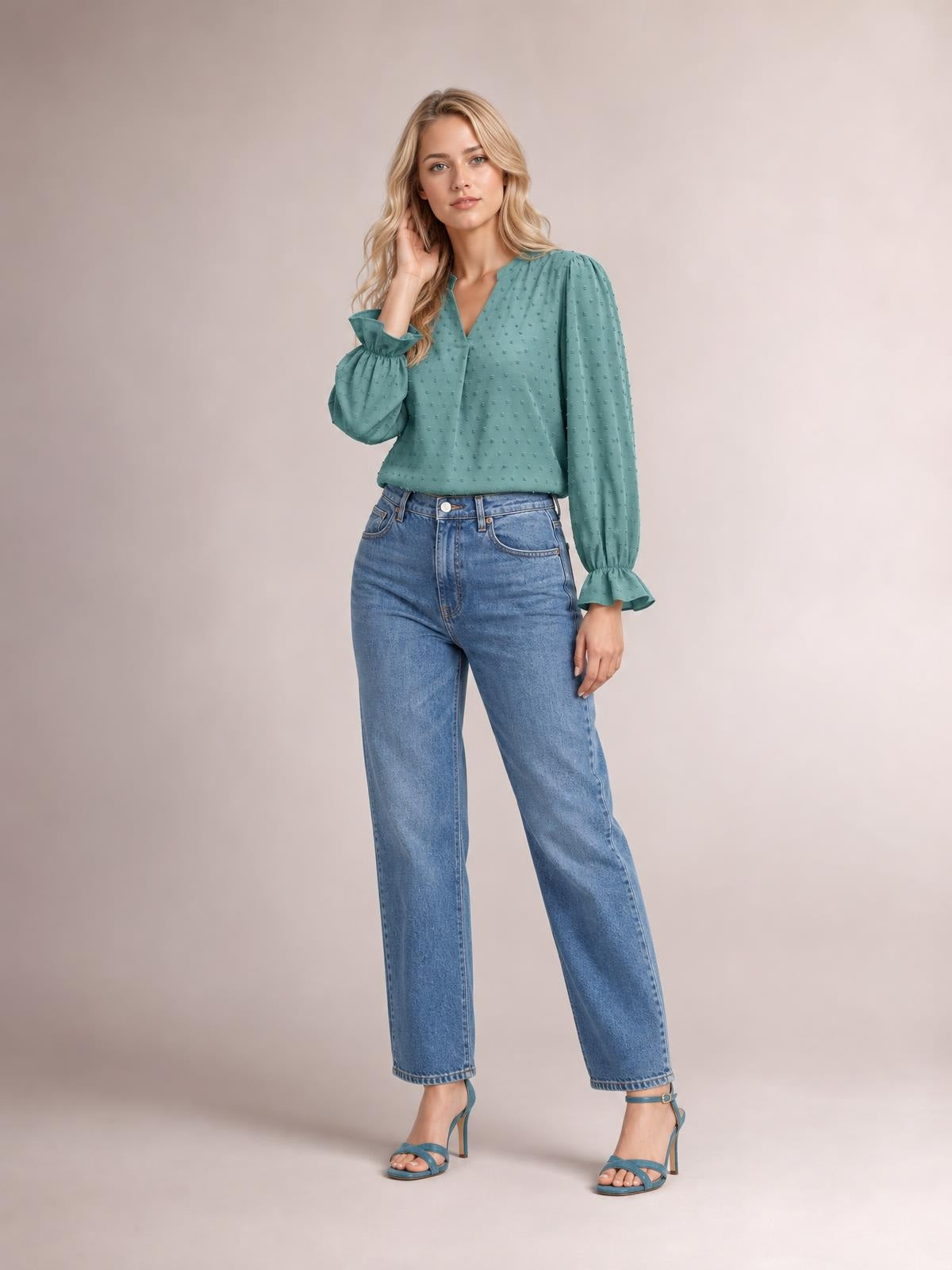 A model poses with one hand in her hair wearing a teal Swiss dot blouse with a notched V-neck, relaxed silhouette, and long flounce sleeves.
