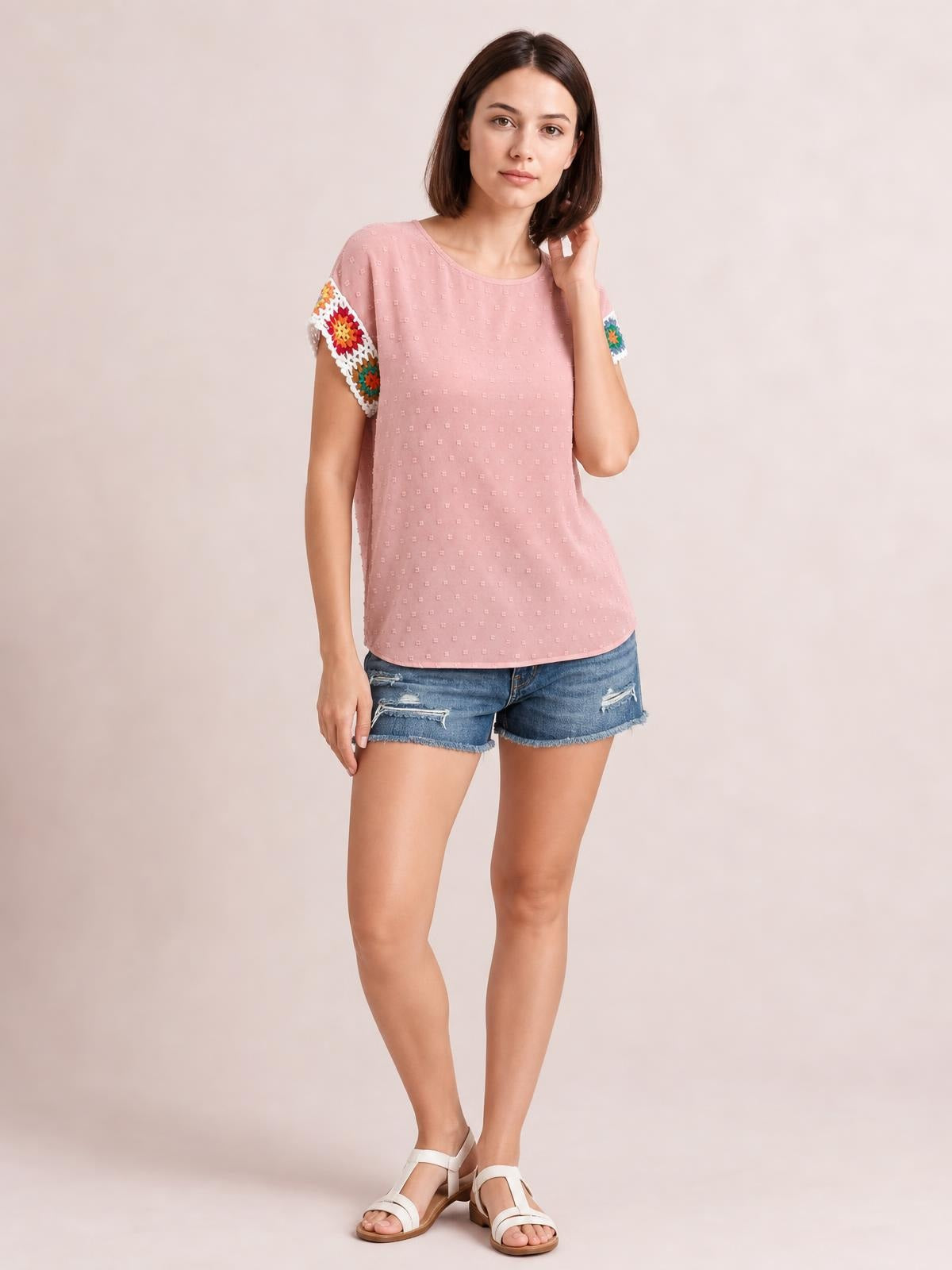 Model wearing a pink Swiss dot top with a round neck, short crochet sleeves with colorful floral accents, and a relaxed straight silhouette.