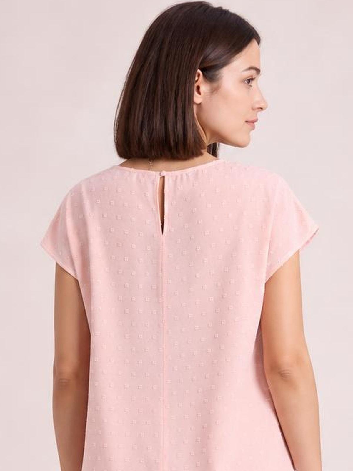 Model shown from the back wearing a pink Swiss dot crochet top with a round neck, short sleeves, relaxed silhouette, and buttoned keyhole closure.