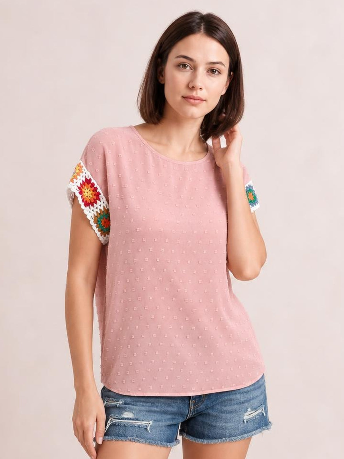 Model wearing a pink Swiss dot round neck crochet short sleeve top with colorful embroidered floral sleeve panels and a relaxed, straight silhouette.
