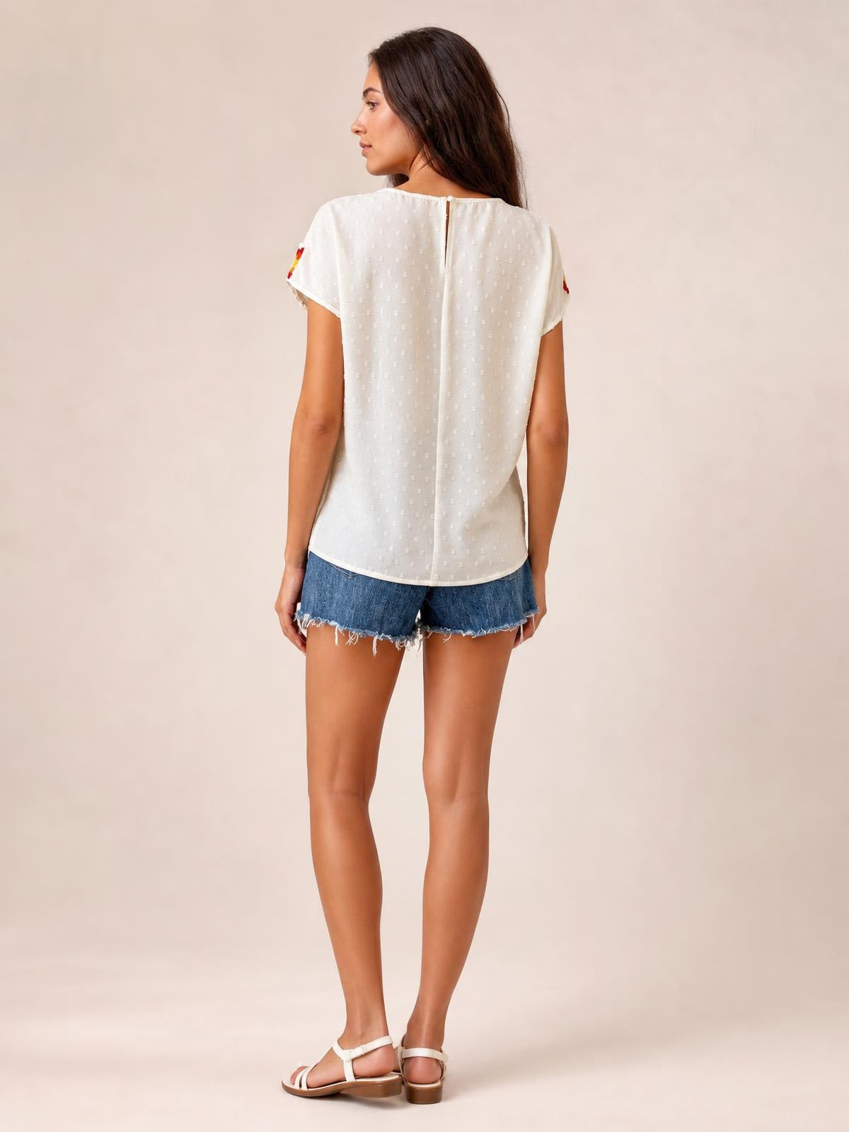A model stands in a white Swiss dot round-neck crochet short-sleeve top with a buttoned back, relaxed silhouette, and curved hem.