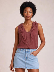 Model wears a mauve Swiss dot tank with wide ruffled straps, a V-neck, front buttons, and a relaxed silhouette, posing with one hand in her pocket.