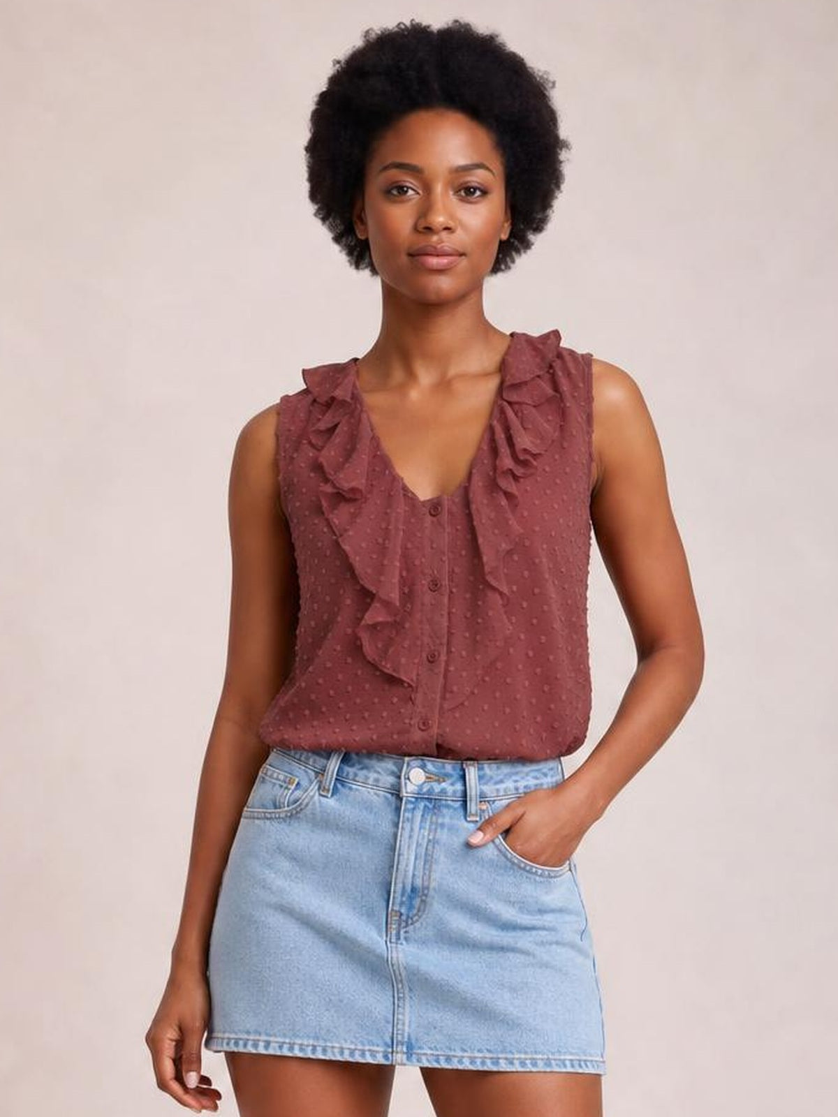 Model wears a mauve Swiss dot tank with wide ruffled straps, a V-neck, front buttons, and a relaxed silhouette, posing with one hand in her pocket.