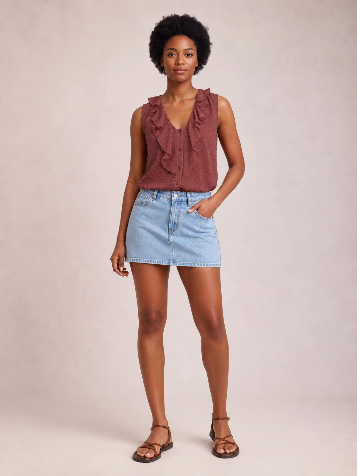 A model wears a burgundy Swiss dot tank with wide ruffled straps, a V-neckline, button-front construction, and a relaxed silhouette, posing with one hand in her pocket.