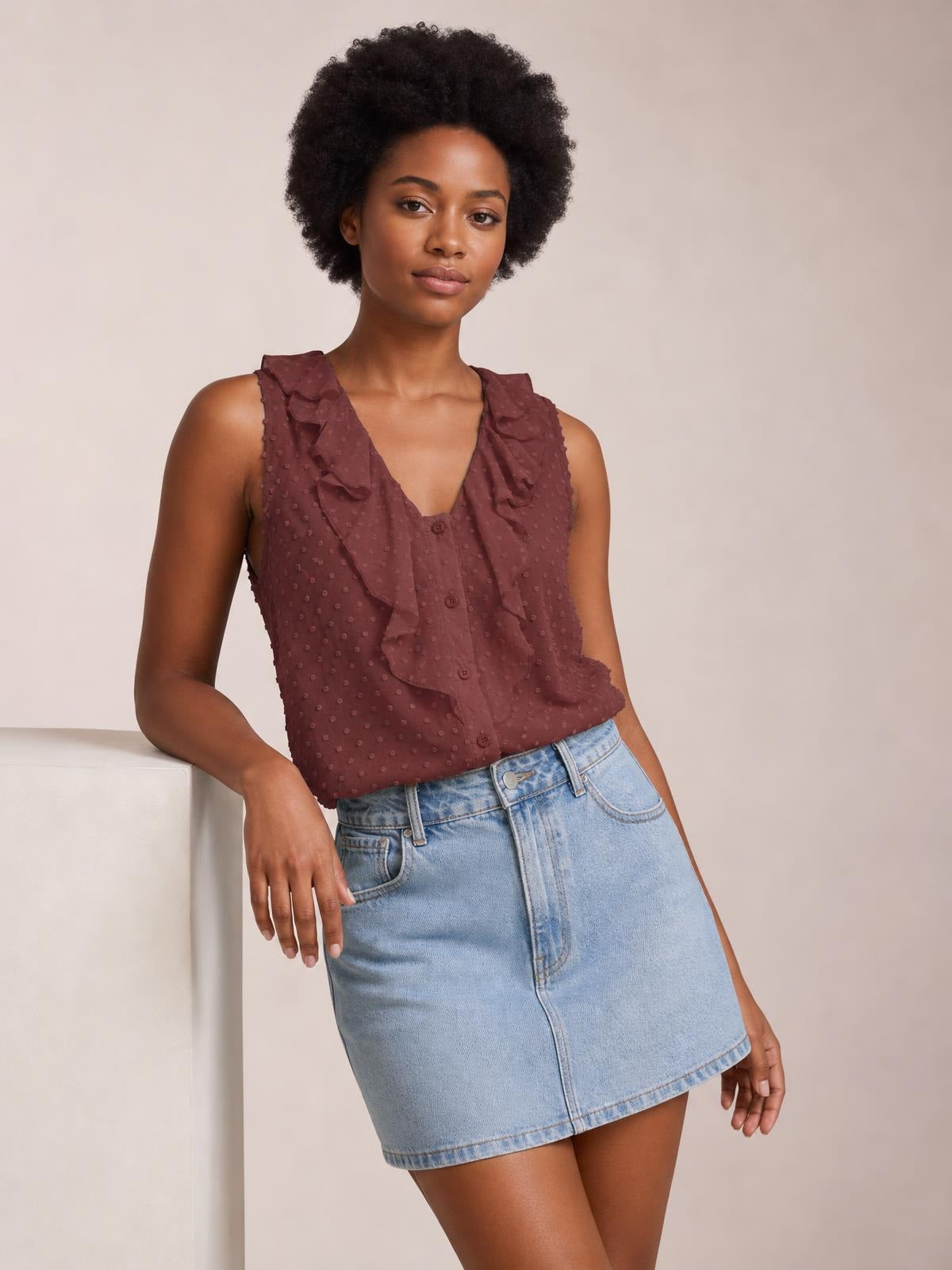 A model leans casually in a burgundy Swiss dot tank with wide straps, layered ruffled trim, a V-neckline, button-front construction, and a relaxed silhouette.