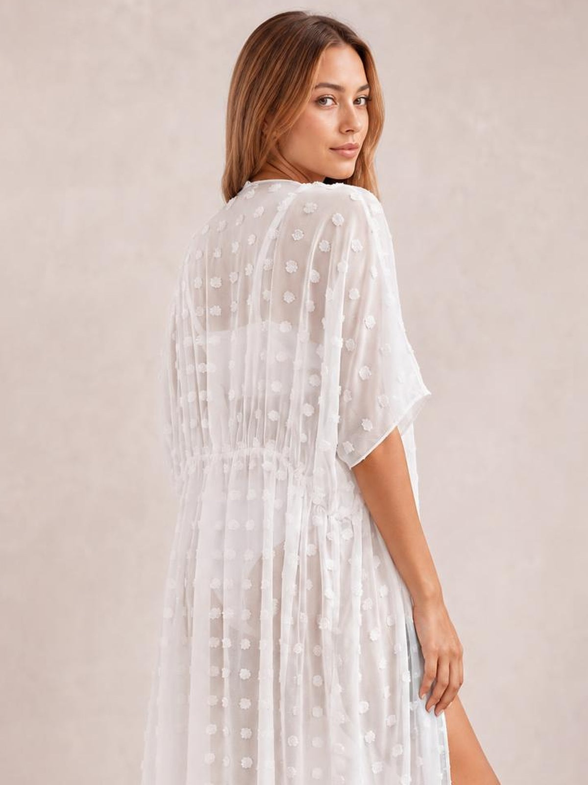 Model looks over her shoulder in a white sheer Swiss dot beach cover up maxi dress with short sleeves, a loose silhouette, and side split.