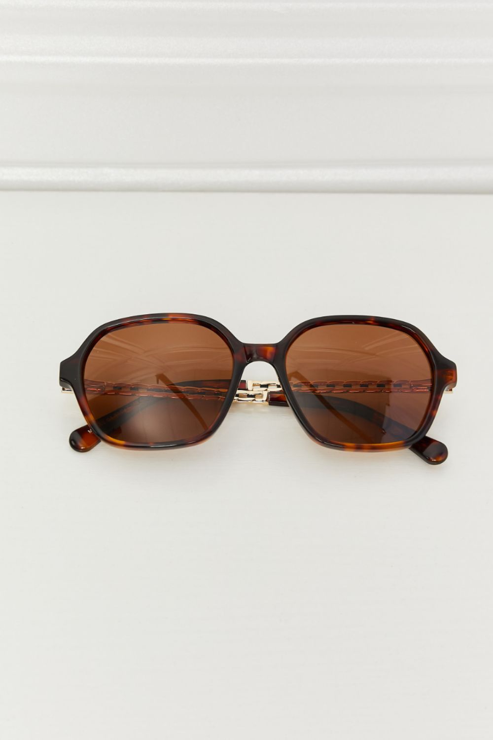Brown full-rim sunglasses with softly rounded square frames, warm brown lenses, and sculpted acetate temples accented with visible metal details.