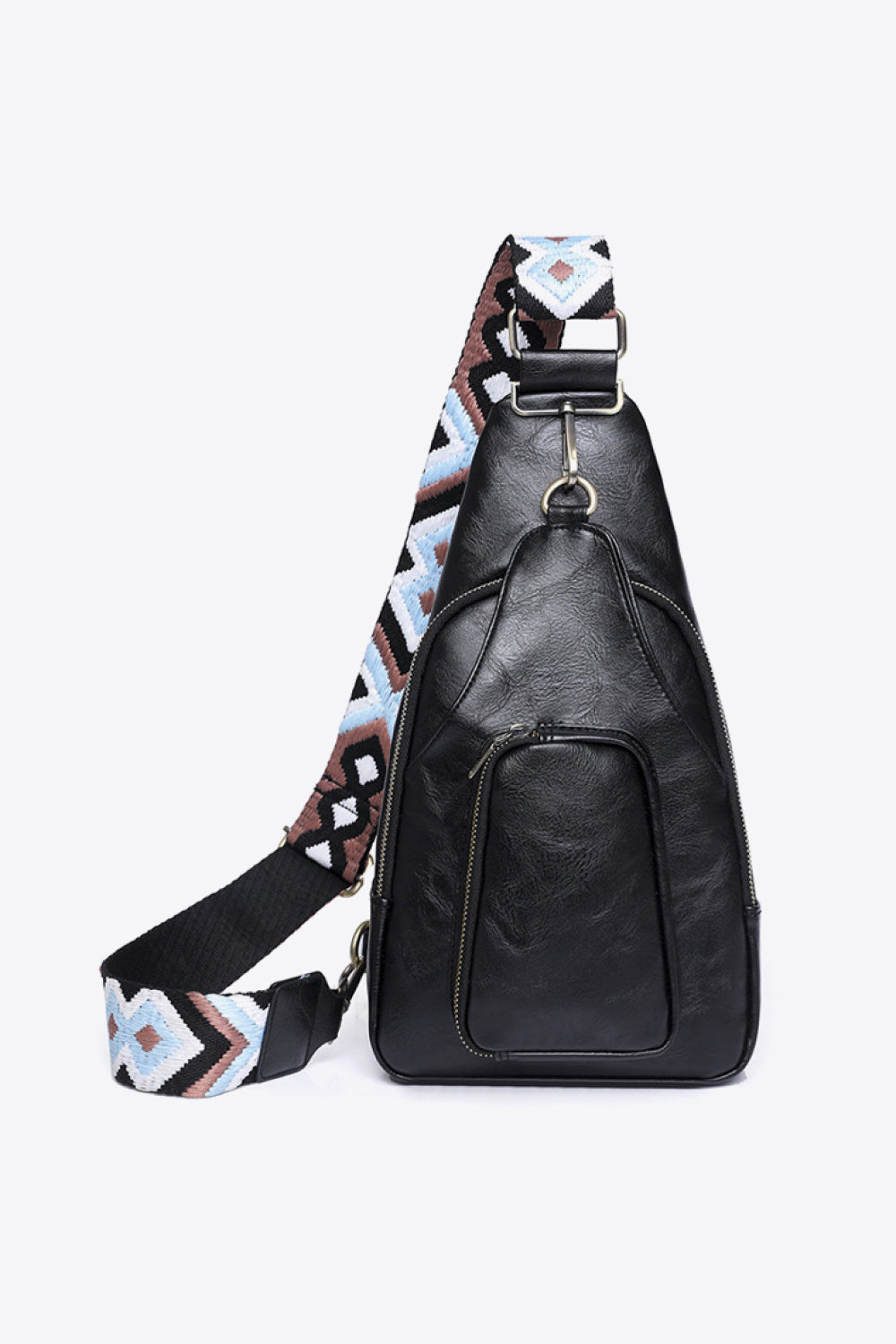 Black PU leather Take A Trip sling bag with a structured triangular silhouette, broad patterned strap, metal hardware, and a large front zip pocket.