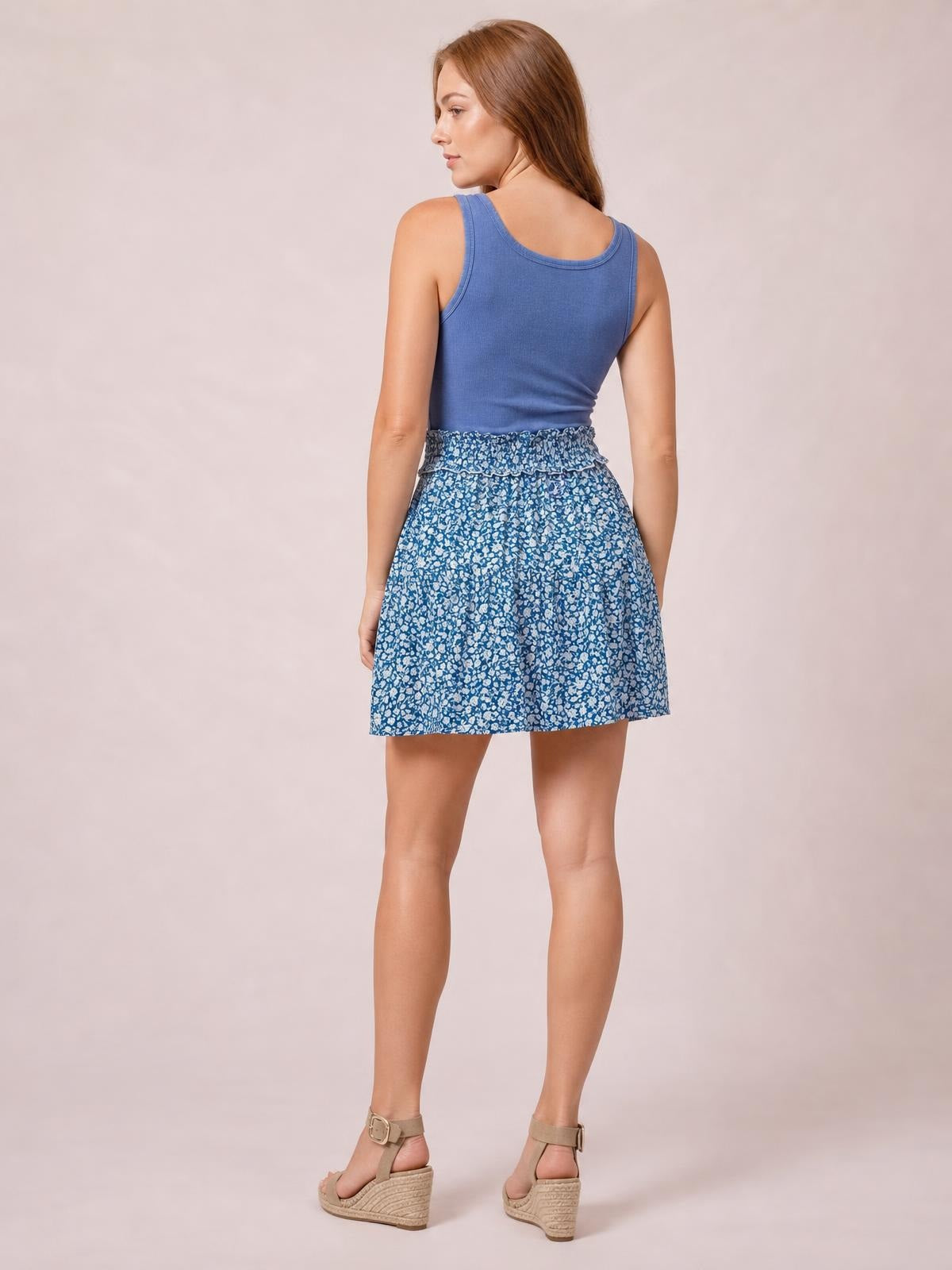 A model turns away to show the blue floral Tassel Mini Skirt’s gathered waistband and relaxed, flared mini silhouette.