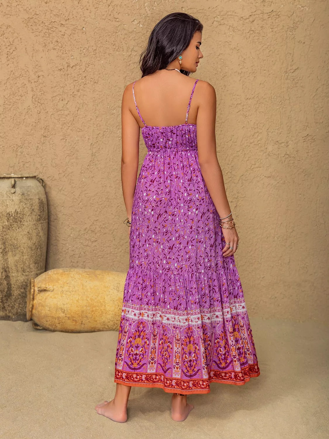Model shown from behind in a heliotrope purple floral print cami dress with thin straps, ruched bodice, flowing tiered maxi silhouette, and decorative bordered hem.