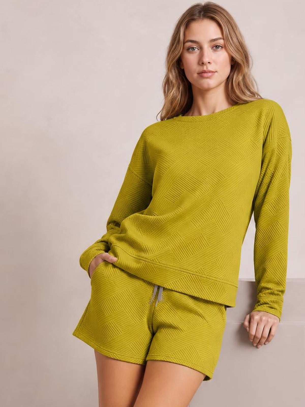 Model in a relaxed pose wears a mustard textured long sleeve top with an oversized silhouette and matching drawstring shorts.