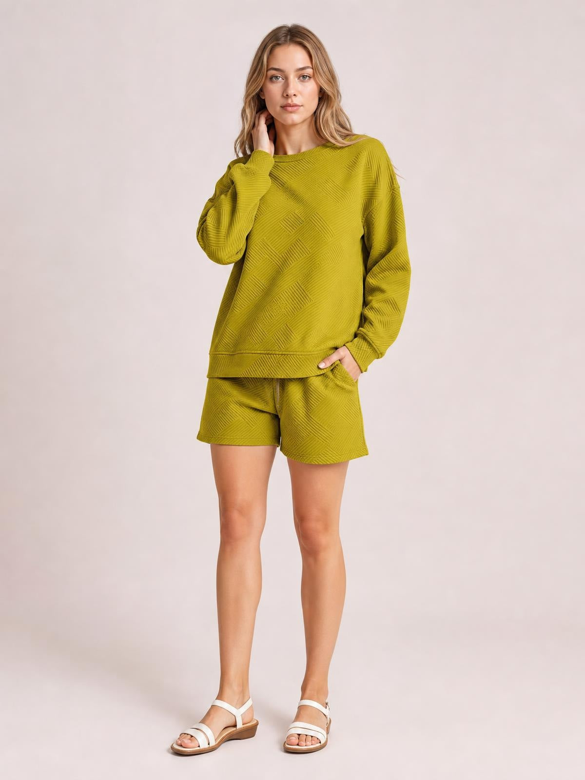 A model poses in an olive green textured long sleeve top and drawstring shorts set with a relaxed silhouette, geometric pattern, ribbed trim, and a hand in a pocket.