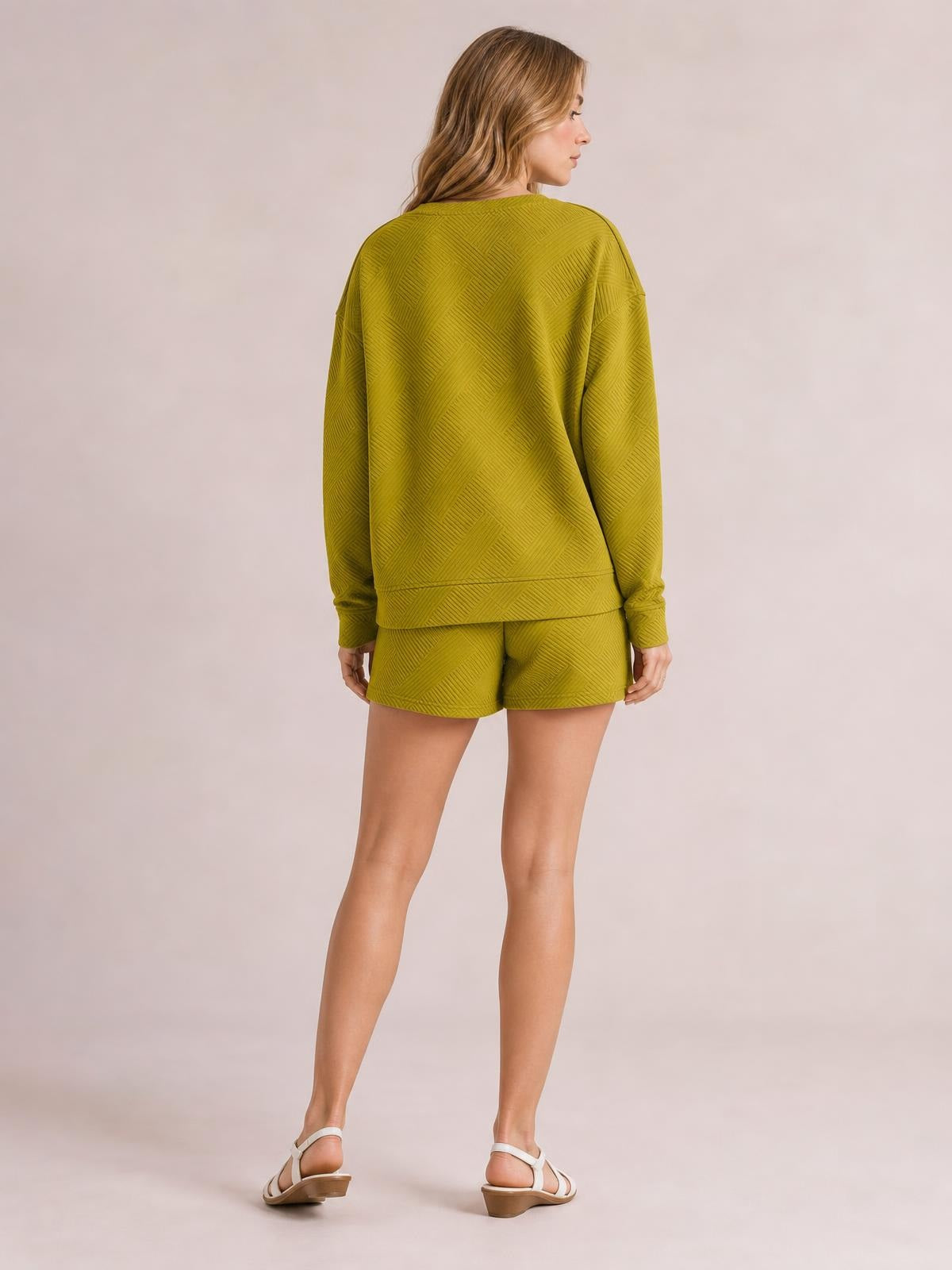 A model poses from the back in an olive green textured long-sleeve top with a relaxed silhouette and matching drawstring shorts.