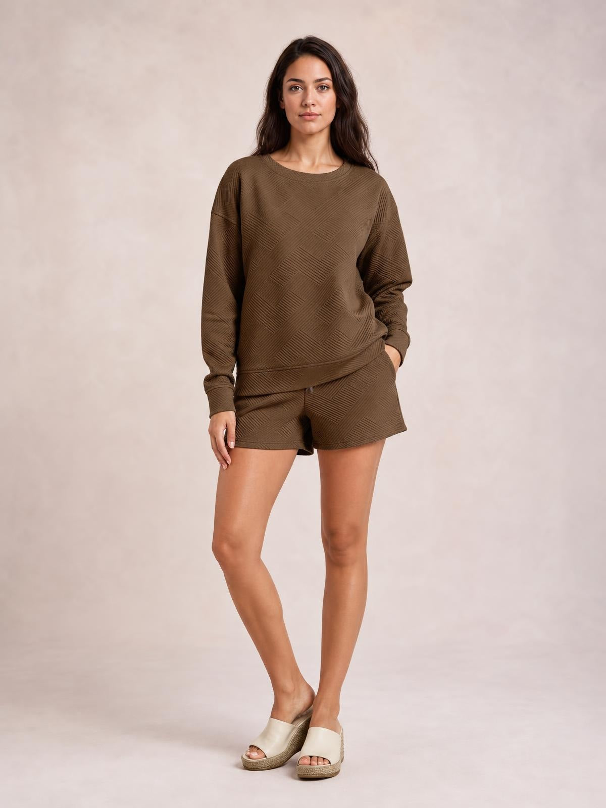 Model wearing a relaxed brown textured long sleeve top and matching drawstring shorts set, standing with one hand in a pocket.