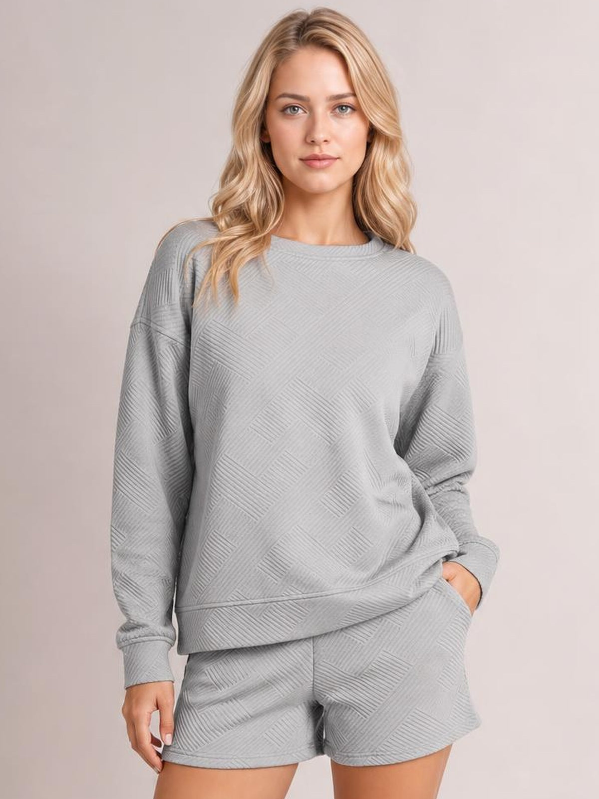 A woman poses in a relaxed gray textured long-sleeve top and matching drawstring shorts set, showing the crew neckline, loose silhouette, and side pockets.