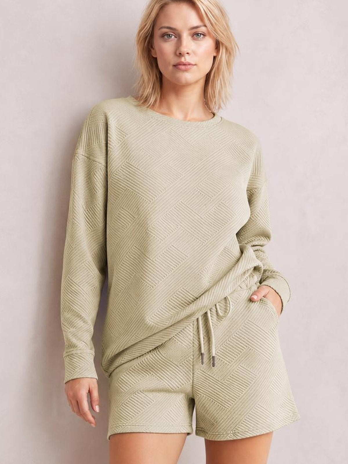 Model poses in a relaxed textured beige long sleeve top and drawstring shorts set, featuring a loose silhouette, geometric pattern, and side pockets.