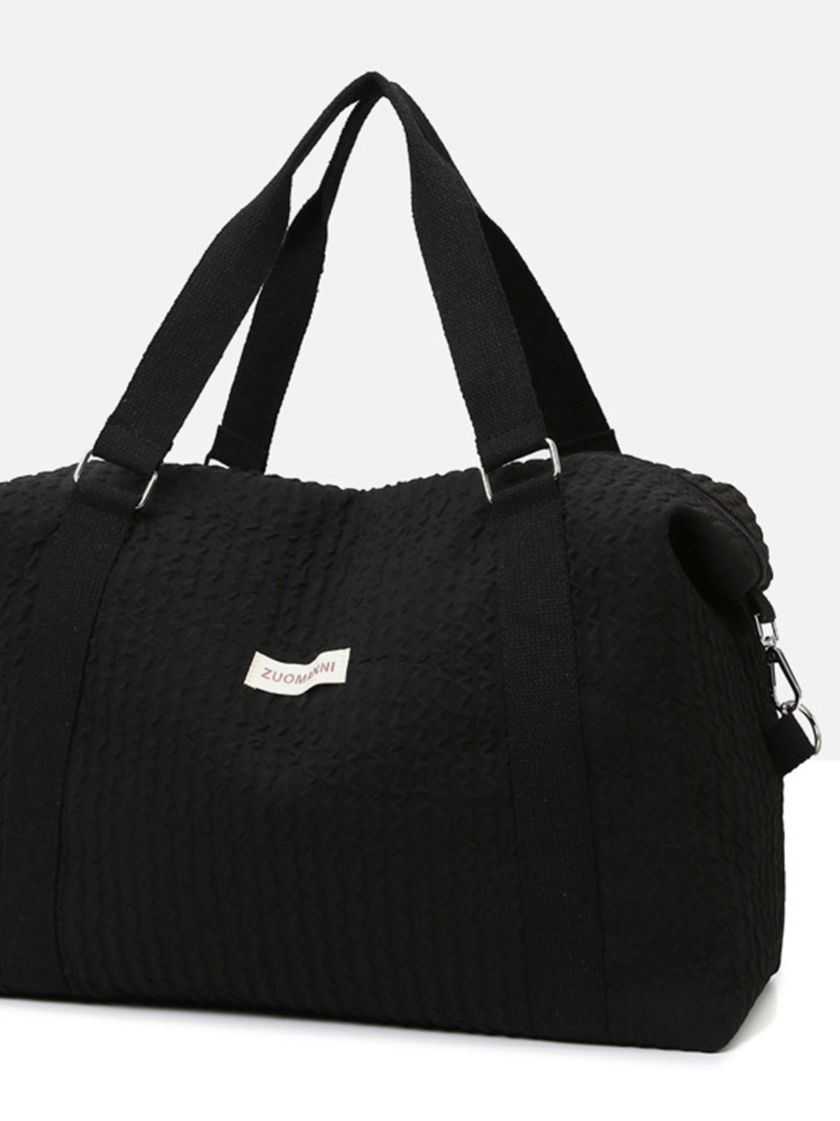 Large black textured Oxford cloth travel bag with a softly structured silhouette, wide top handles, reinforced straps, and a side clip attachment.