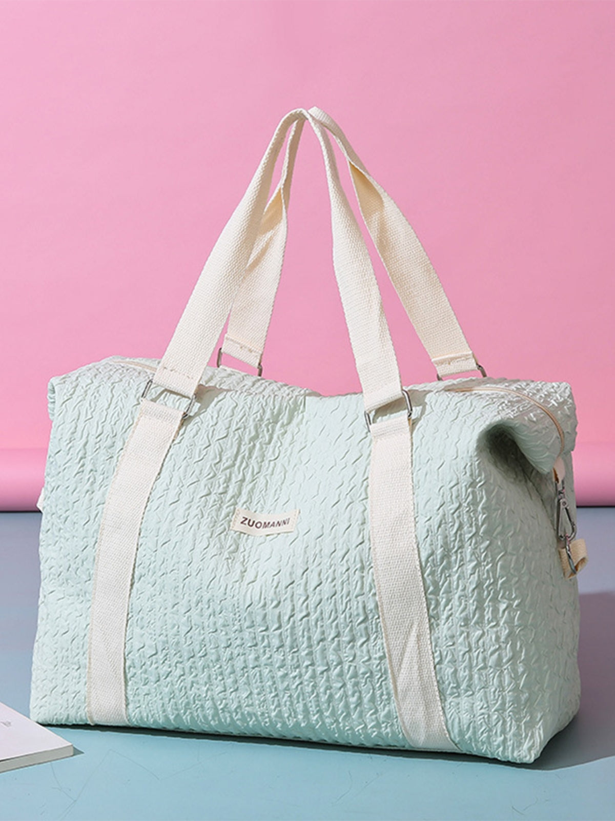 A large mint-green textured Oxford cloth travel bag with a softly structured silhouette, wide cream top handles, and a zippered top opening.