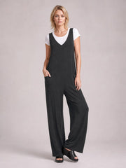 A model poses in a black textured sleeveless jumpsuit with a V-neck, wide-leg silhouette, front pockets, and a white T-shirt layered underneath.