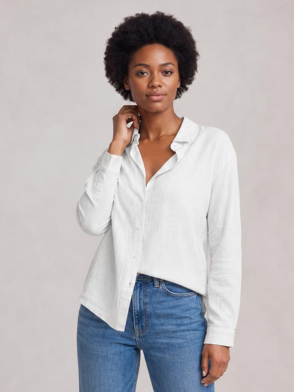Model wearing a white textured button-front shirt with a collared neckline, long regular sleeves, relaxed silhouette, and curved hem, touching the collar.