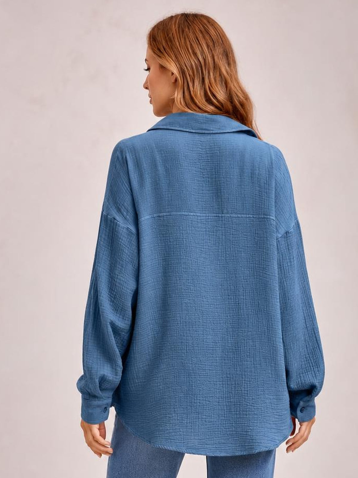 A model shows the back of a blue textured longline shirt with a collared neckline, dropped shoulders, long sleeves, and a relaxed oversized silhouette.