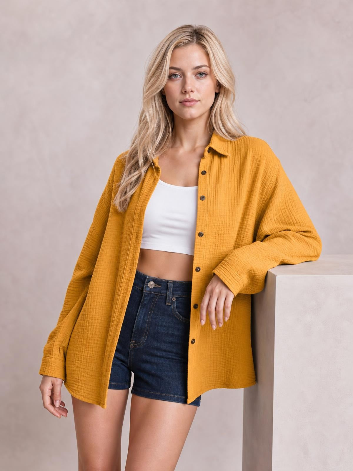 A model wears a mustard textured dropped-shoulder longline shirt with a collared neckline, button front, long sleeves, and a relaxed silhouette while leaning.