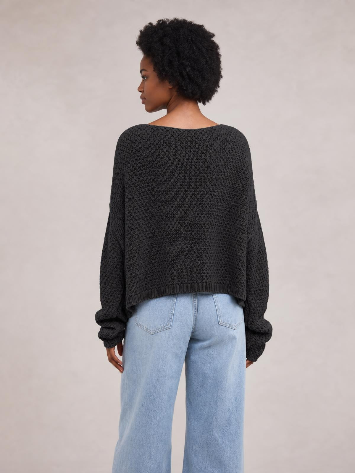Model shown from behind wearing a black textured knit round neck sweater with a relaxed oversized silhouette, long sleeves, ribbed cuffs, and hem.