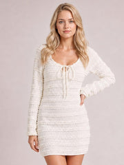 A model poses in a white textured long-sleeve bodycon mini dress with a tie-front neckline, exposed seams, and a fitted silhouette.