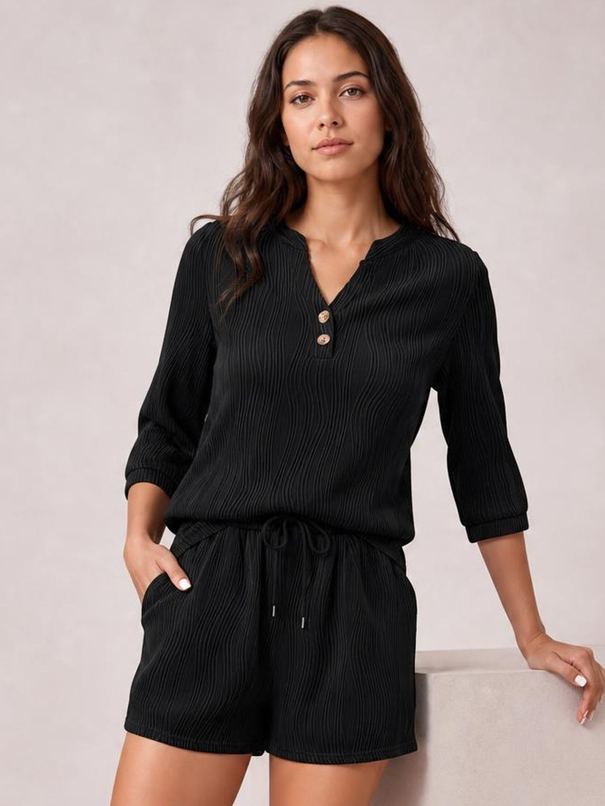 Model wearing a black textured notched long-sleeve top and drawstring shorts set, featuring a relaxed silhouette, button placket, and pockets.