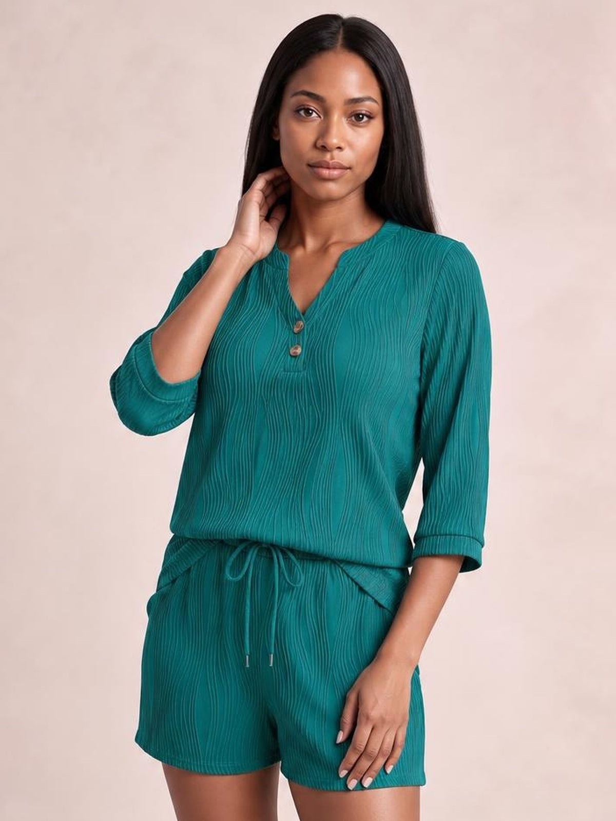 Model poses in a teal textured top and drawstring shorts set featuring a notched neckline, three-quarter sleeves, relaxed silhouette, and pockets.