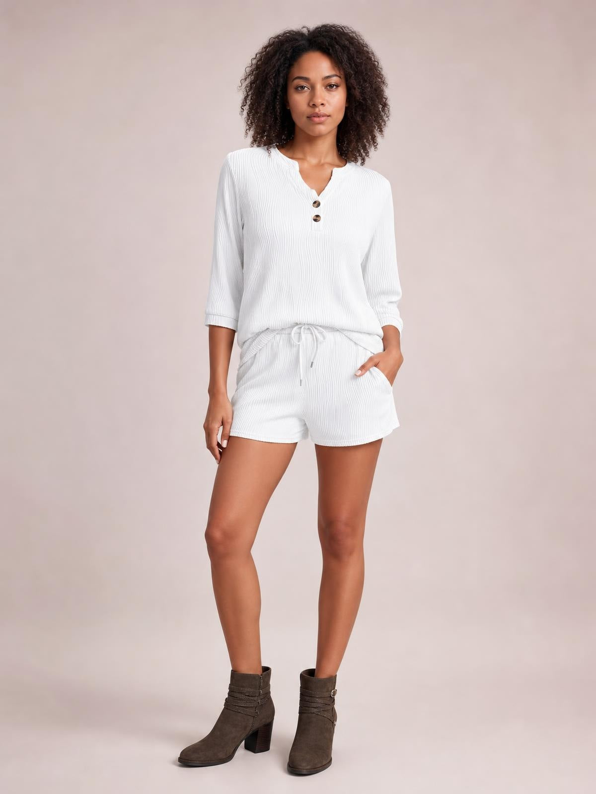 A model stands in a white textured notched top and drawstring shorts set, featuring a relaxed silhouette, button placket, three-quarter sleeves, and pockets.