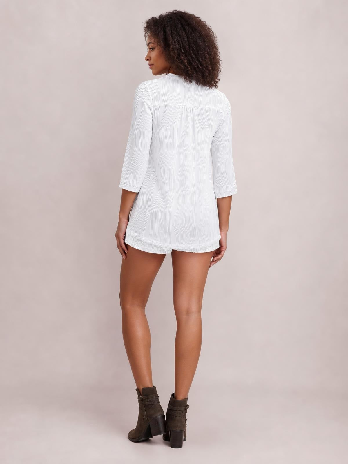 Model poses turned away in a white textured notched top and drawstring shorts set with a relaxed silhouette, three-quarter sleeves, and shorts pockets.