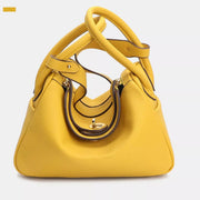 Small yellow textured PU leather handbag with a structured trapezoid silhouette, twin rounded handles, dark contrast trim, and a gold-tone front clasp.