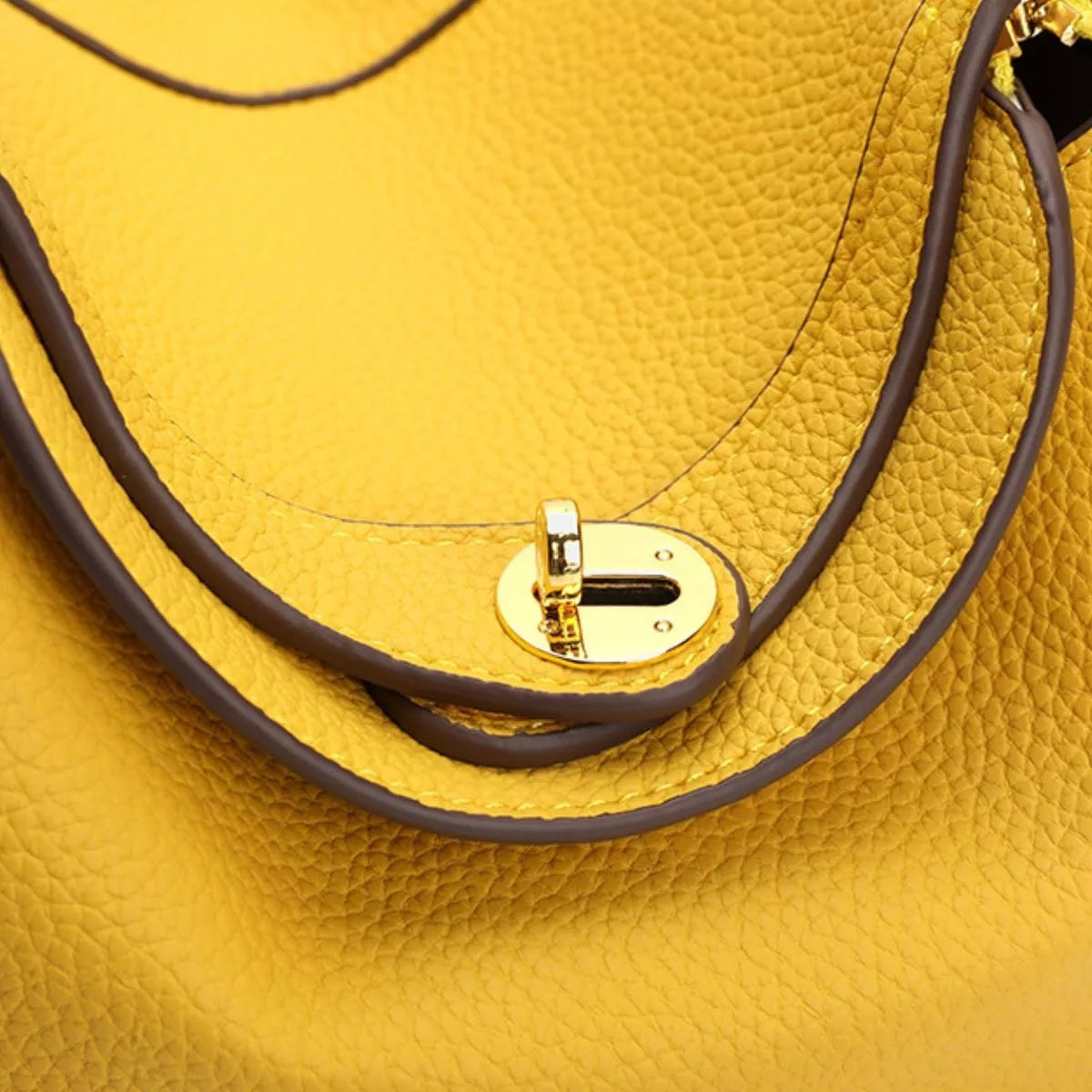 Close-up of a small yellow textured PU leather handbag featuring dark brown trim, a slim strap, and a polished gold turn-lock closure.