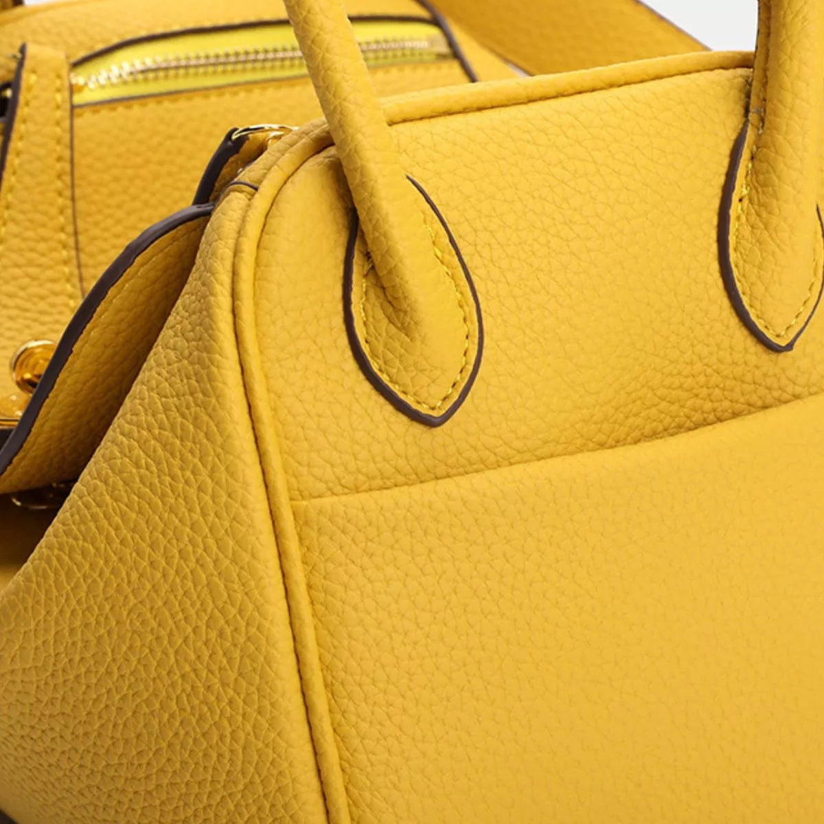 Small mustard-yellow textured PU leather handbag with a structured silhouette, dual top handles, dark edge piping, and neatly stitched panel construction.