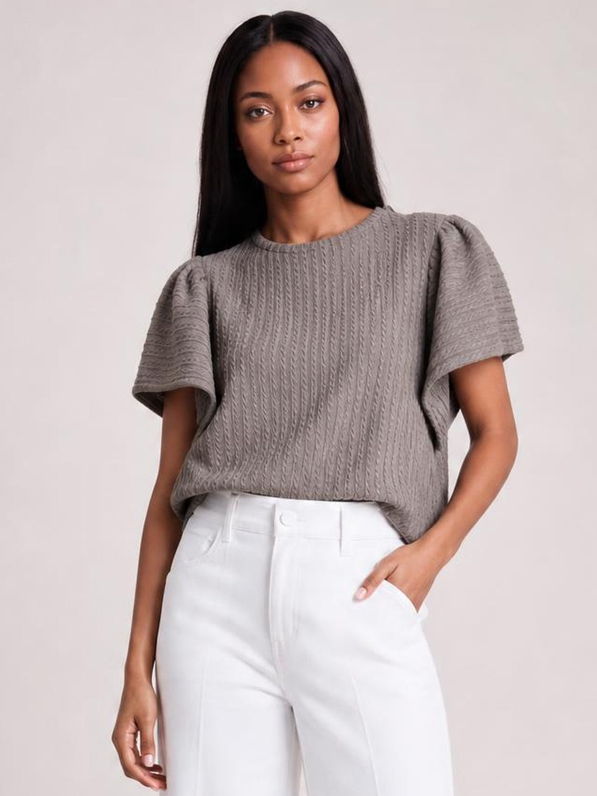 Model wears a gray textured round neck blouse with flounce sleeves, a relaxed straight silhouette, and slight stretch, paired with white pants.