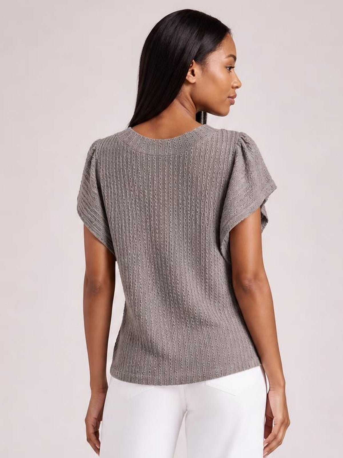 Model shown from the back in a gray textured blouse with a round neck, flounce sleeves, and a relaxed straight silhouette.