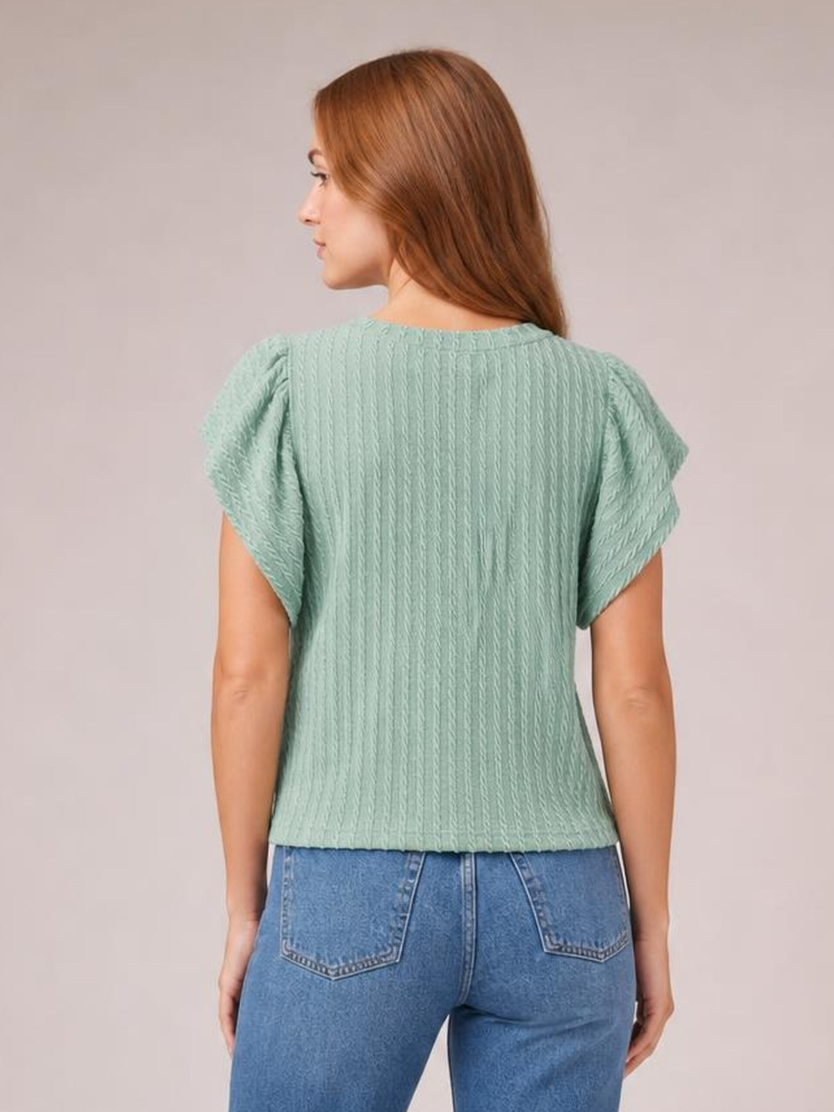 A model is shown from the back wearing a mint green textured round neck blouse with short flounce sleeves and a relaxed straight silhouette.