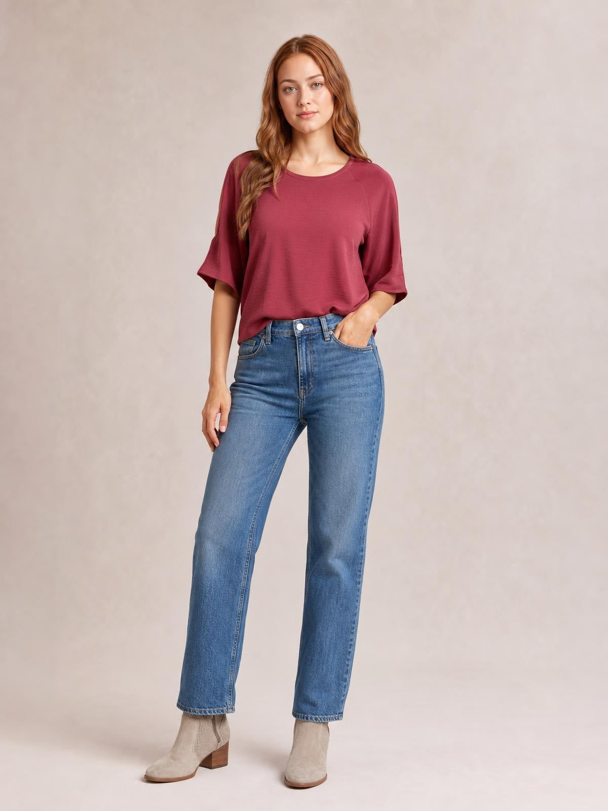 A model poses with one hand in her pocket wearing a burgundy textured round neck top with a relaxed long silhouette and cold-shoulder half sleeves.