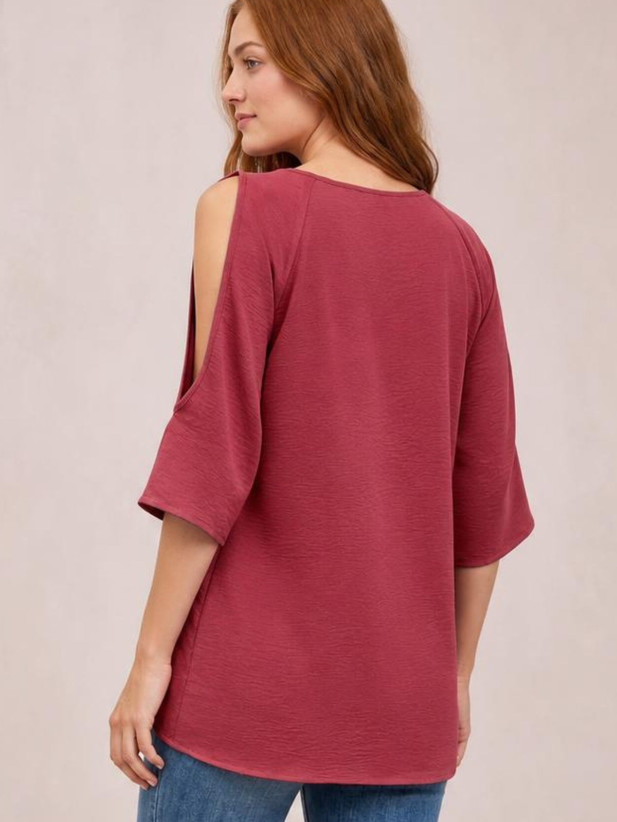 Model shown from behind in a three-quarter pose wearing a burgundy textured round-neck top with cold-shoulder split half sleeves and a relaxed long silhouette.