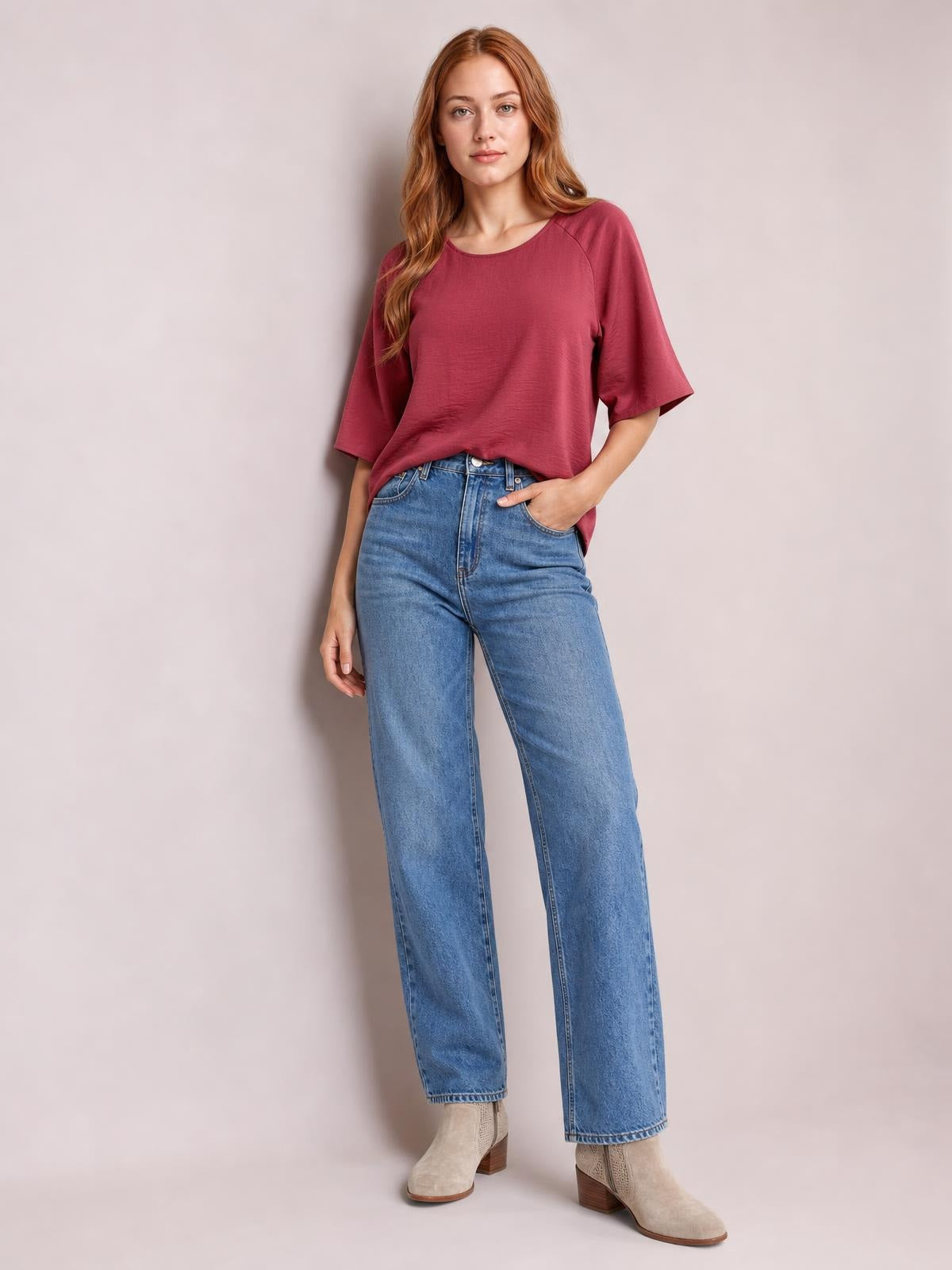 Model wears a burgundy textured round-neck top with a relaxed long silhouette and loose half sleeves, paired with blue jeans and one hand in a pocket.