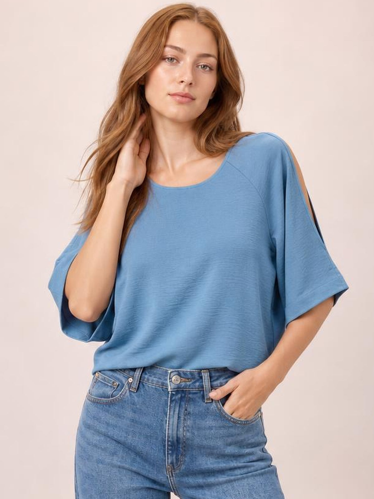 Model wearing a solid blue textured round neck top with a relaxed long silhouette, half-length cold-shoulder split sleeves, and one hand resting near her hair.